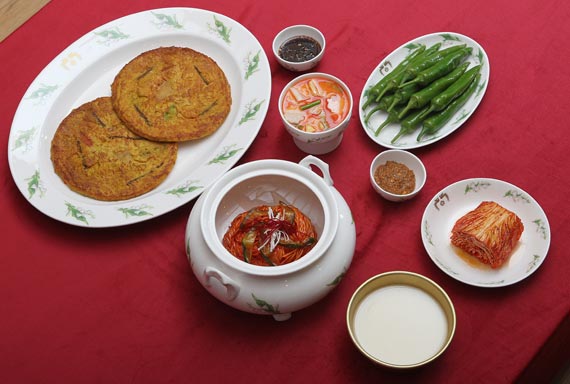 由拌面、马格利酒、辣椒大酱、水泡菜、辣白菜和海鲜葱煎饼组成的加餐桌。 --- 中韩人力网